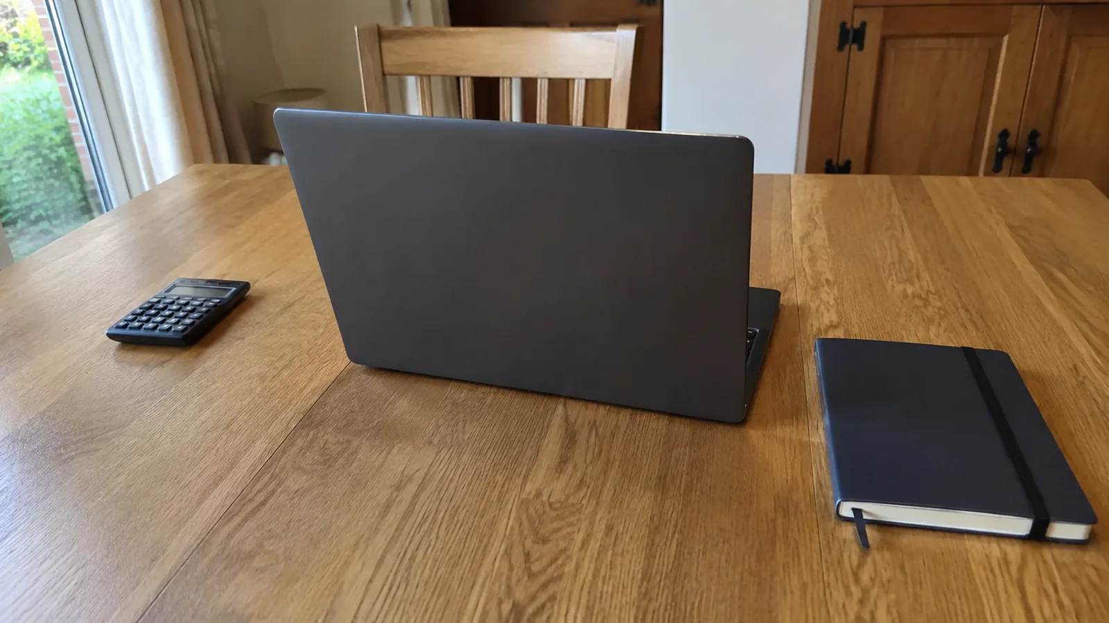 Open laptop sits beside a calculator and notebook on a wooden table.