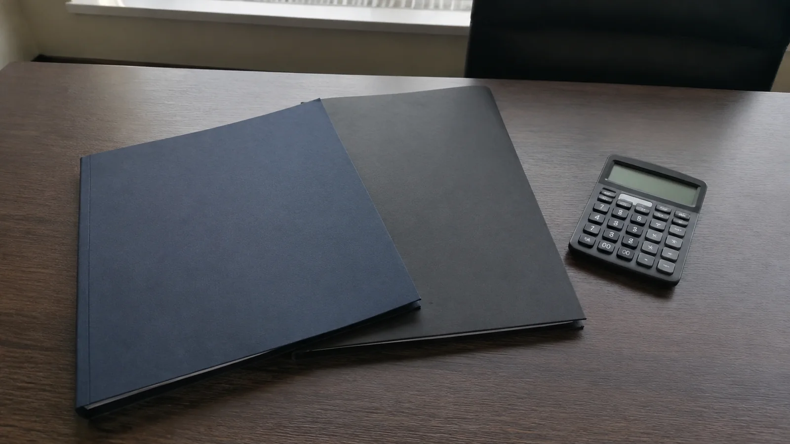 Dark folders and a calculator lie on a wooden surface.