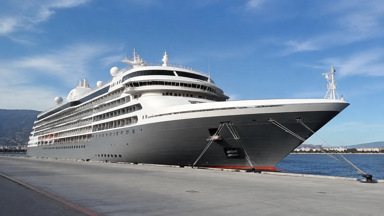 Large cruise ship with a dark hull is moored at a pier.
