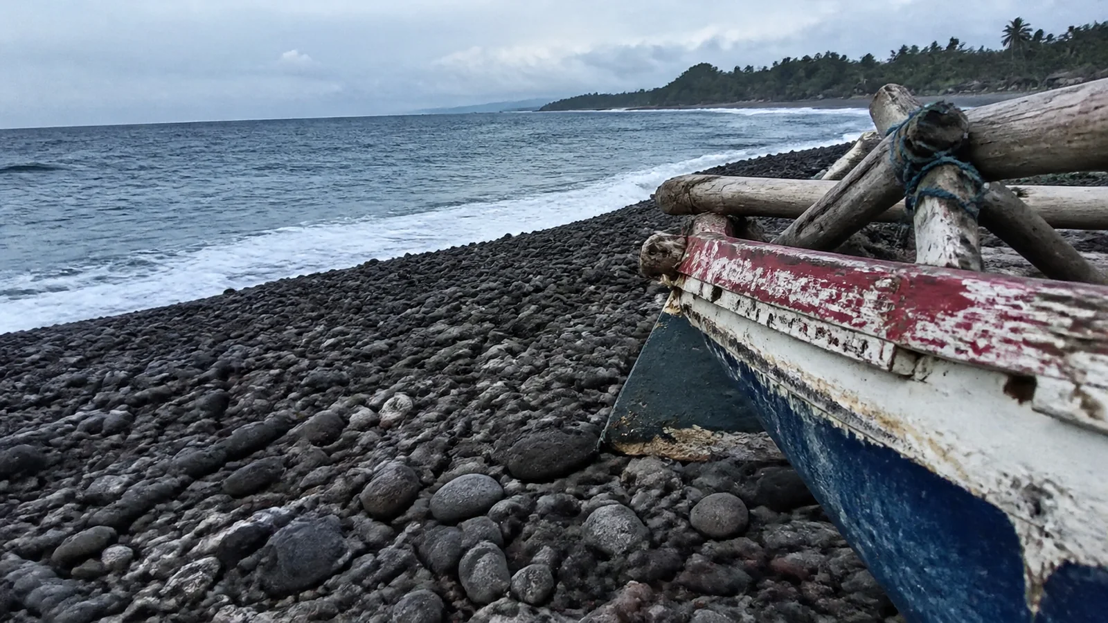 Weathered wooden fishing boat rests on rounded dark beach stones.