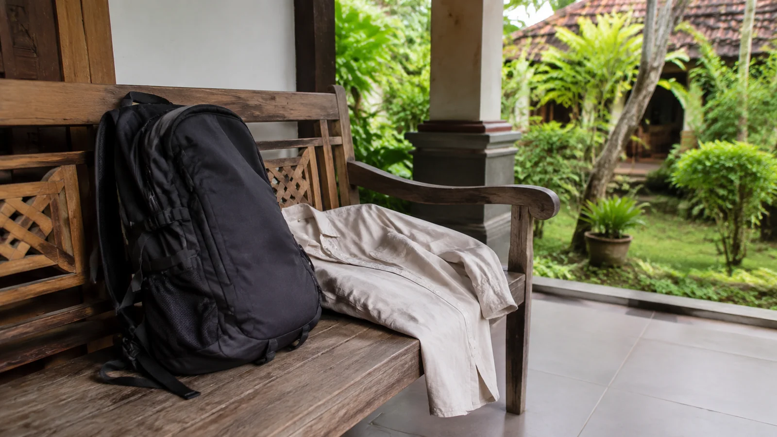 Backpack and light clothing rest on a wooden porch bench.