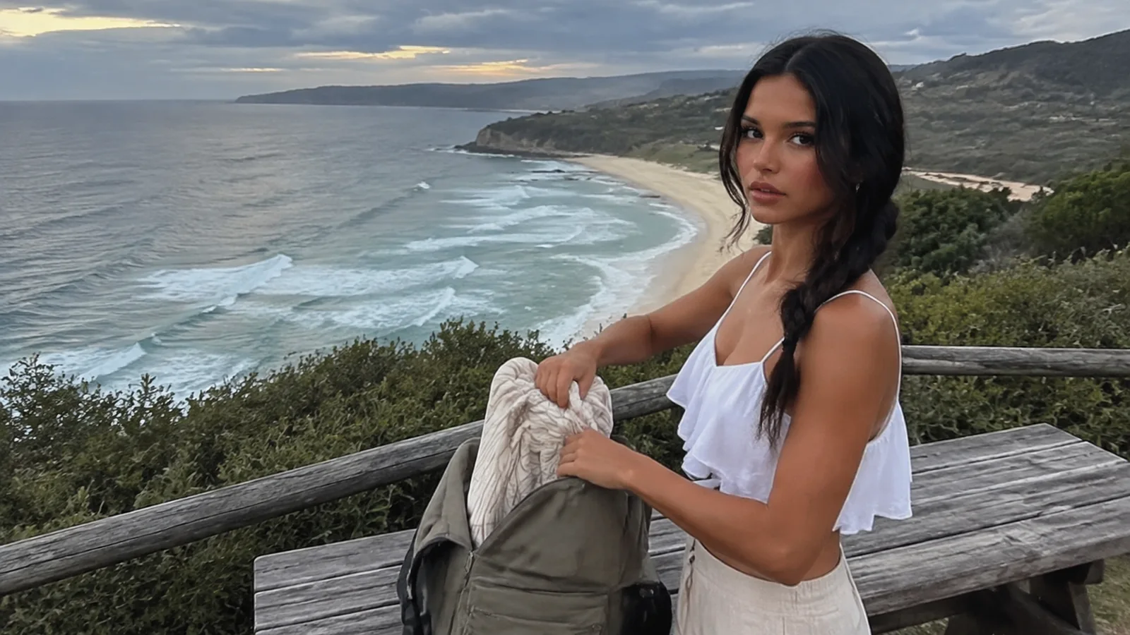 Woman holds a light garment at an overlook above a curving beach.