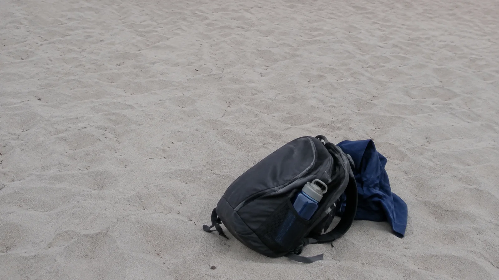 Backpack and blue jacket resting on pale beach sand.