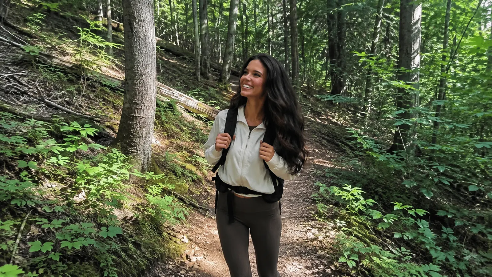 Woman hiking a shaded forest trail with a backpack.