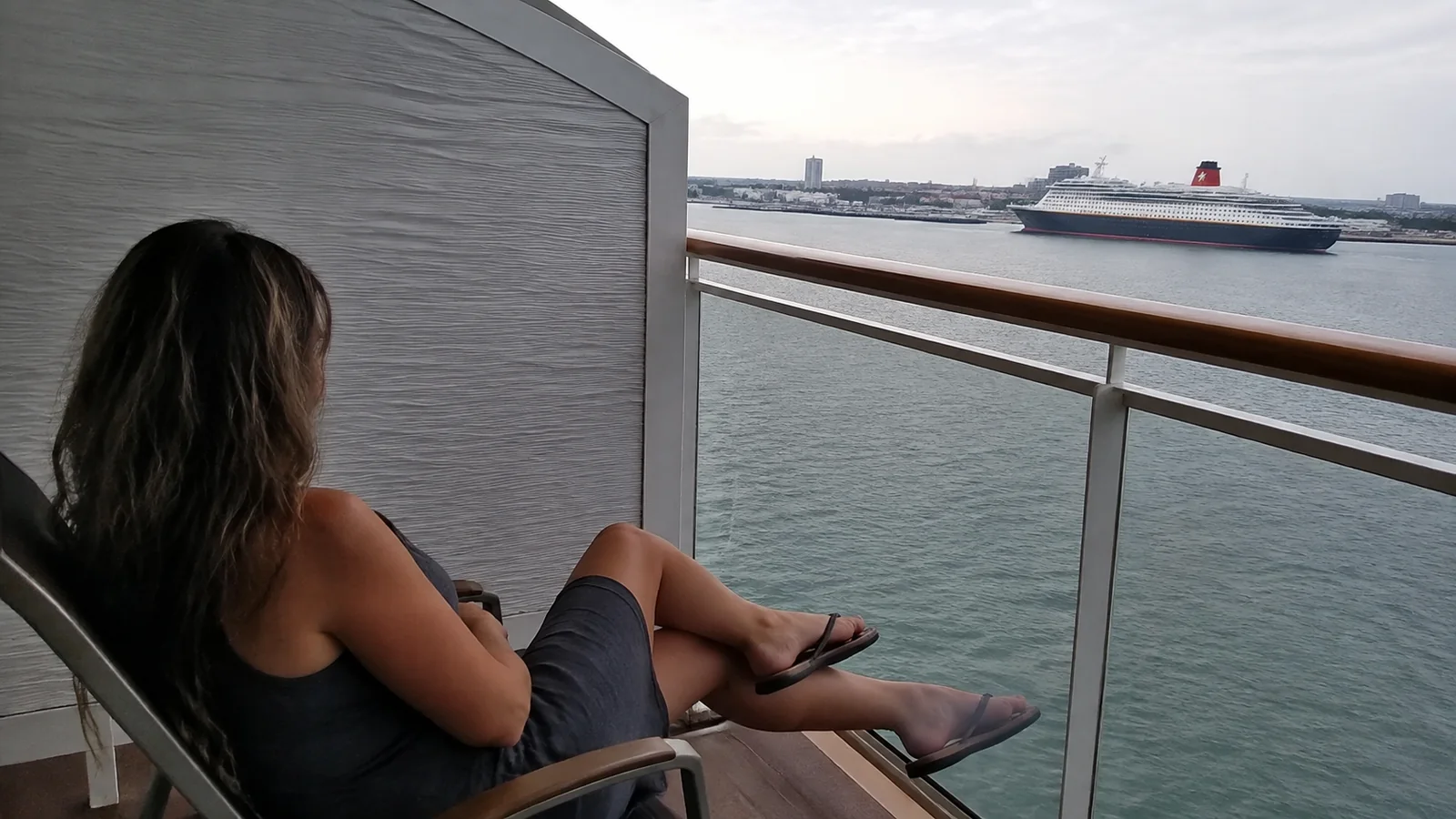 Woman relaxes on a balcony overlooking a harbor and another ship.