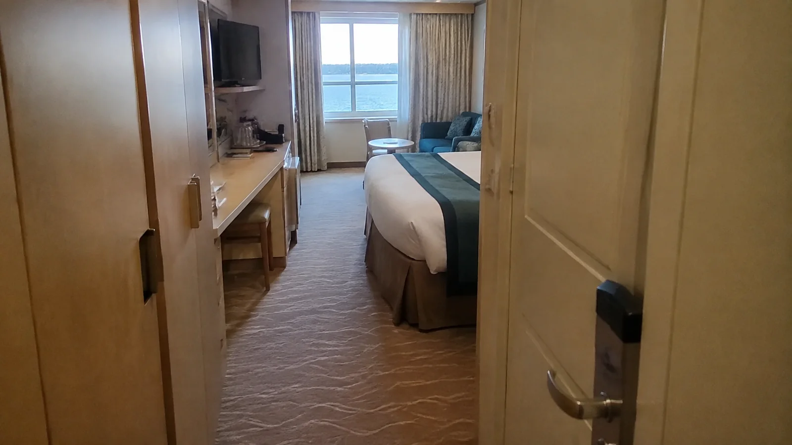 View through a cabin doorway toward a bed and sea-view window.
