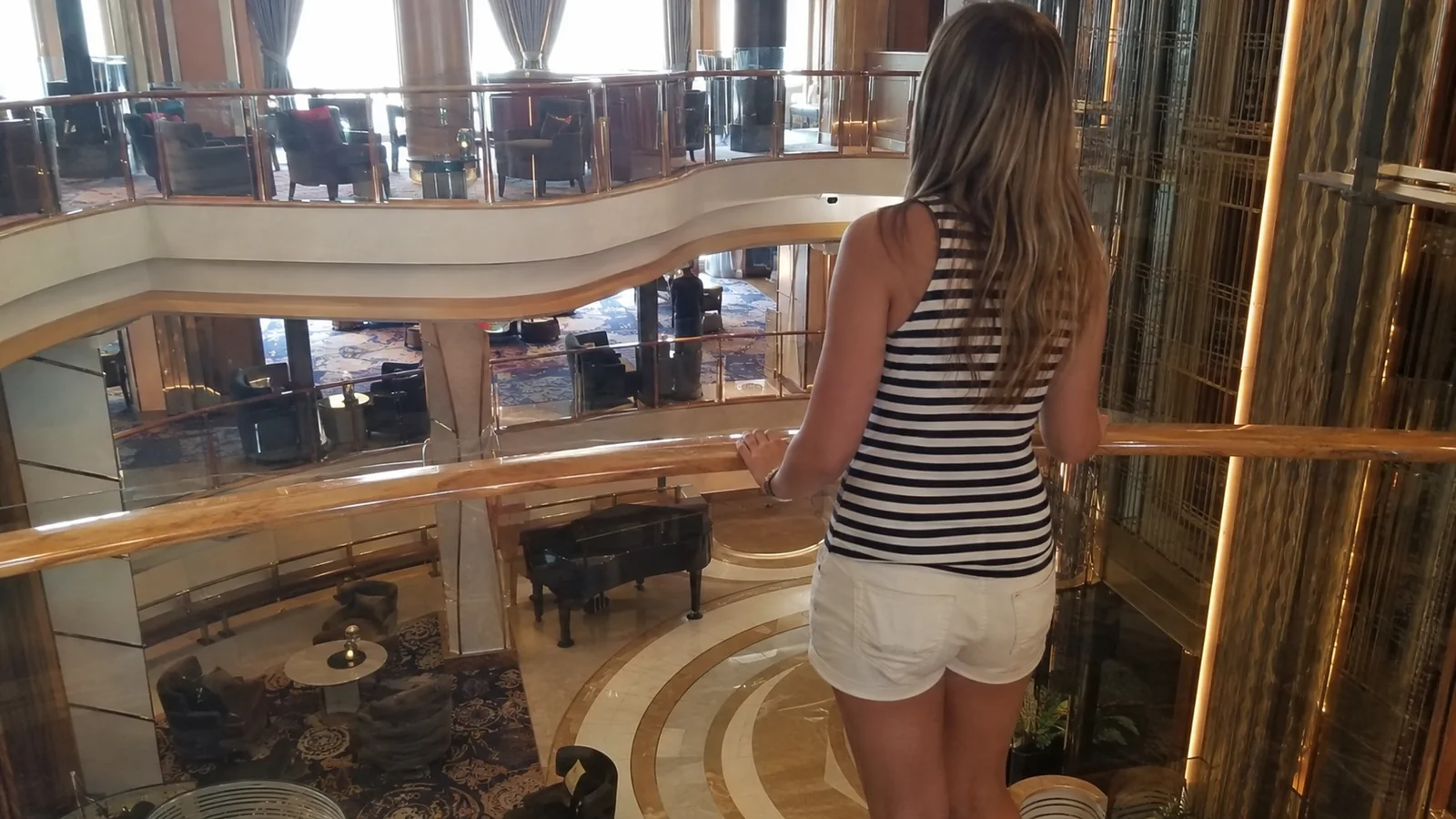 Woman looks over a railing into a multilevel ship atrium.