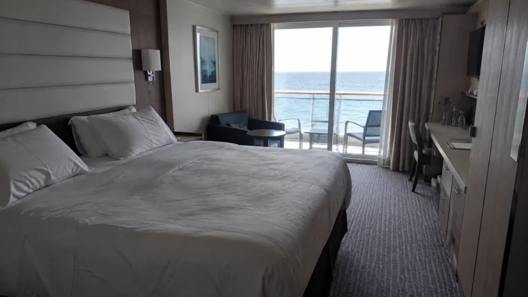 Double bed faces balcony doors in a pale modern stateroom.