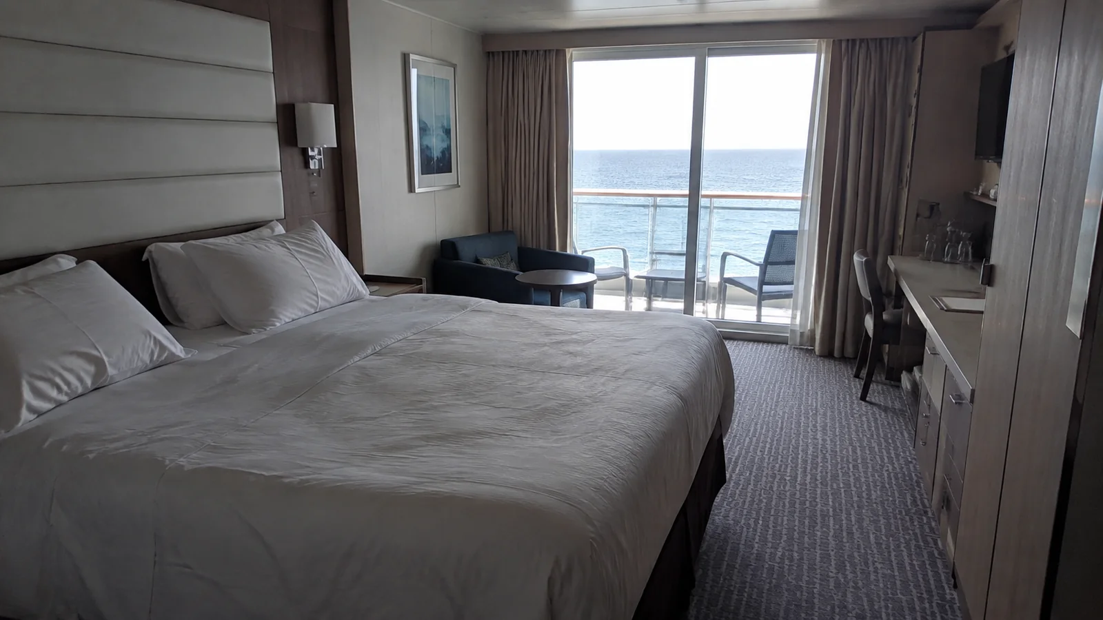 Double bed faces balcony doors in a pale modern stateroom.