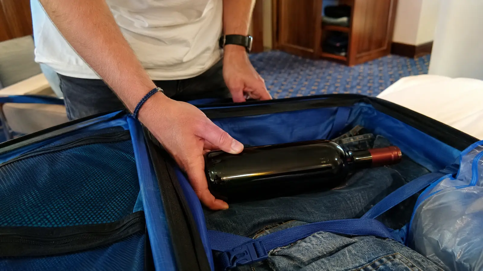Person placing a wine bottle inside an open suitcase
