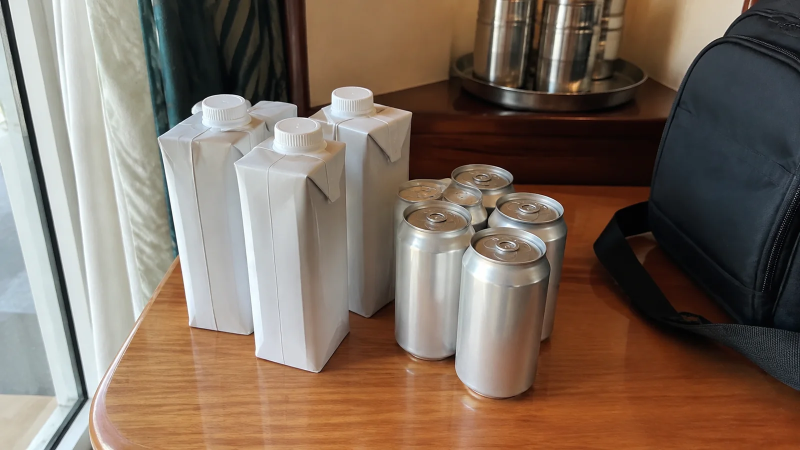 Plain cartons and aluminum cans stand beside a small bag.