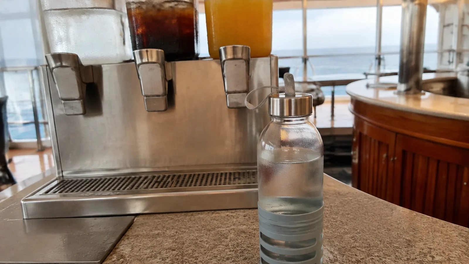 Reusable water bottle stands beside a stainless steel beverage dispenser.
