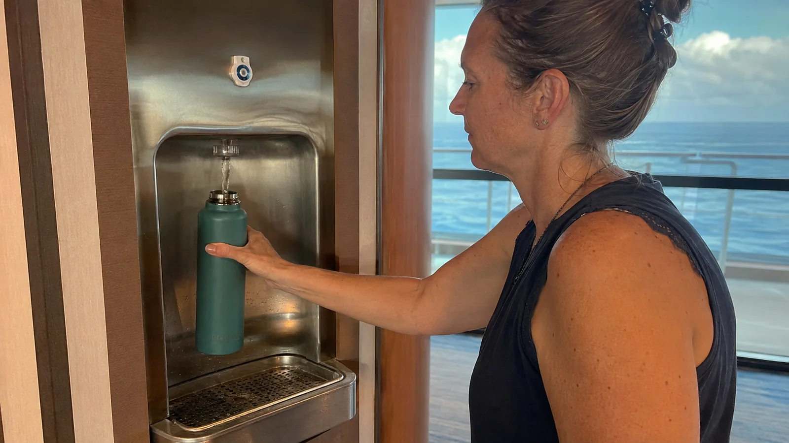 Woman fills a reusable bottle at a recessed water dispenser.