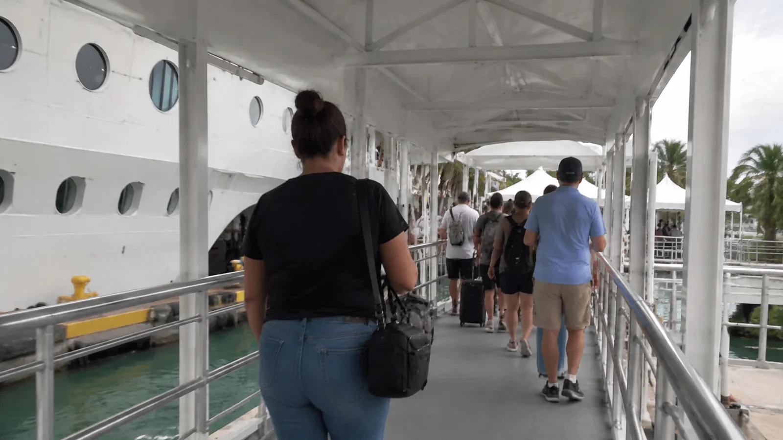 Passengers queue along a covered gangway beside a cruise ship.