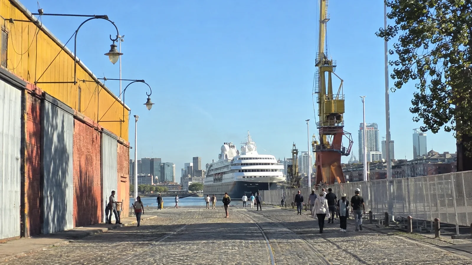 Cruise ship docked at the end of a waterfront street beside port cranes