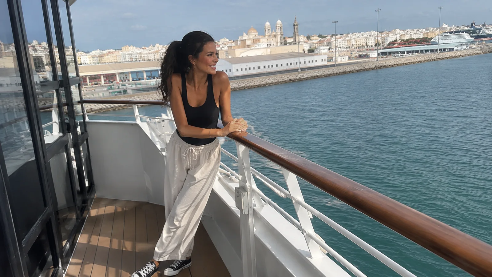 Woman standing on a cruise ship balcony overlooking a harbor
