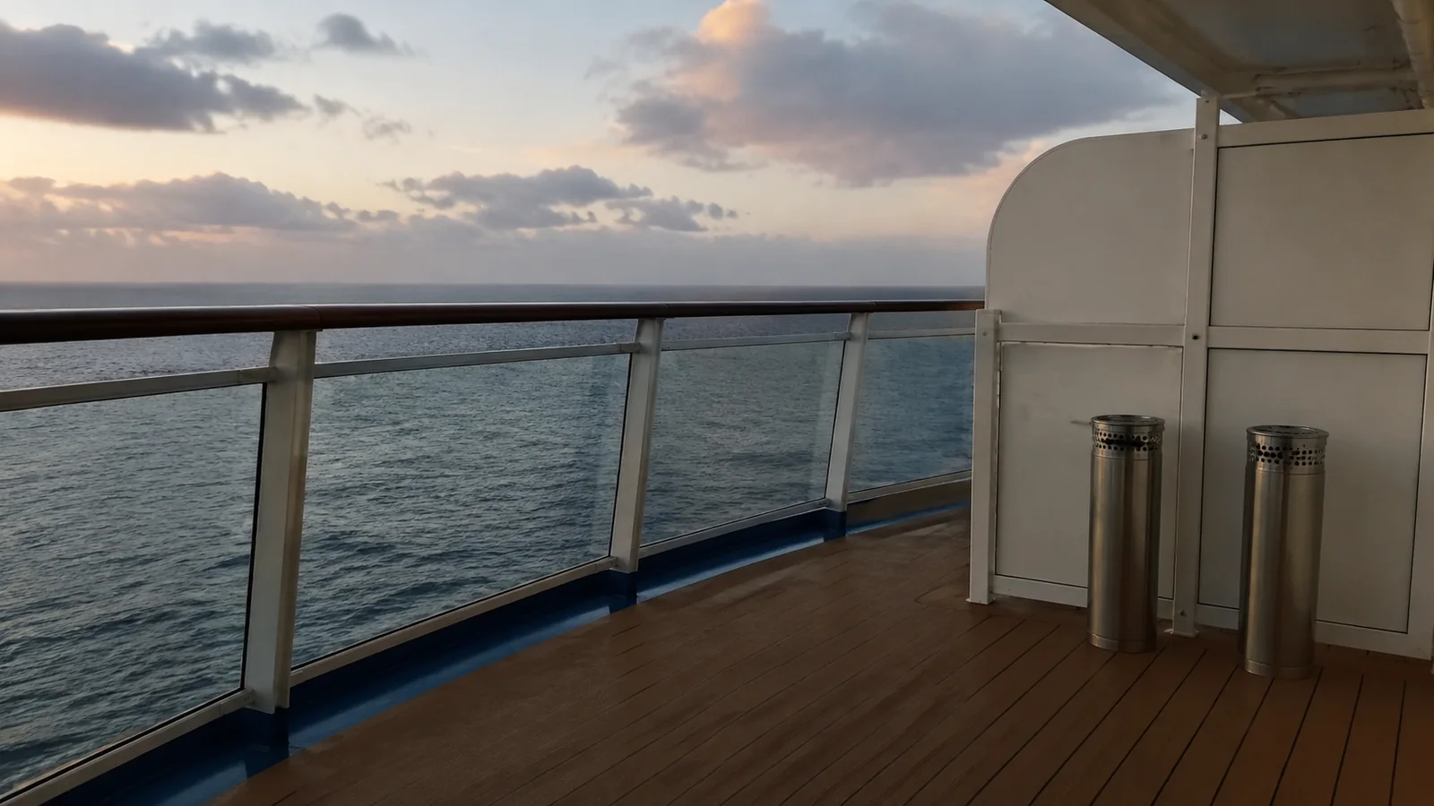 Metal cigarette-disposal bins on a sheltered ship deck at sunset.