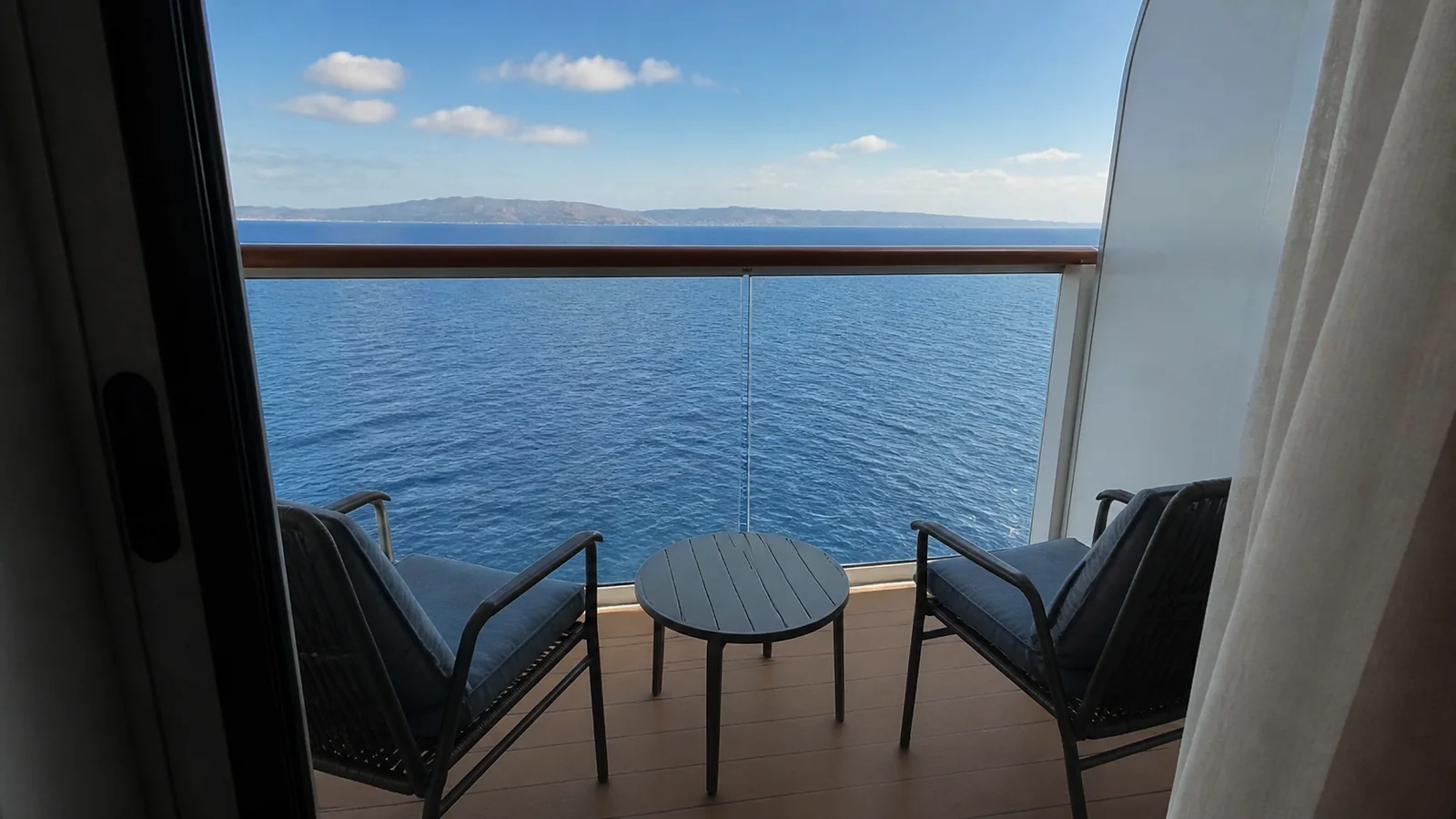 Private cruise cabin balcony with two chairs and a small table.