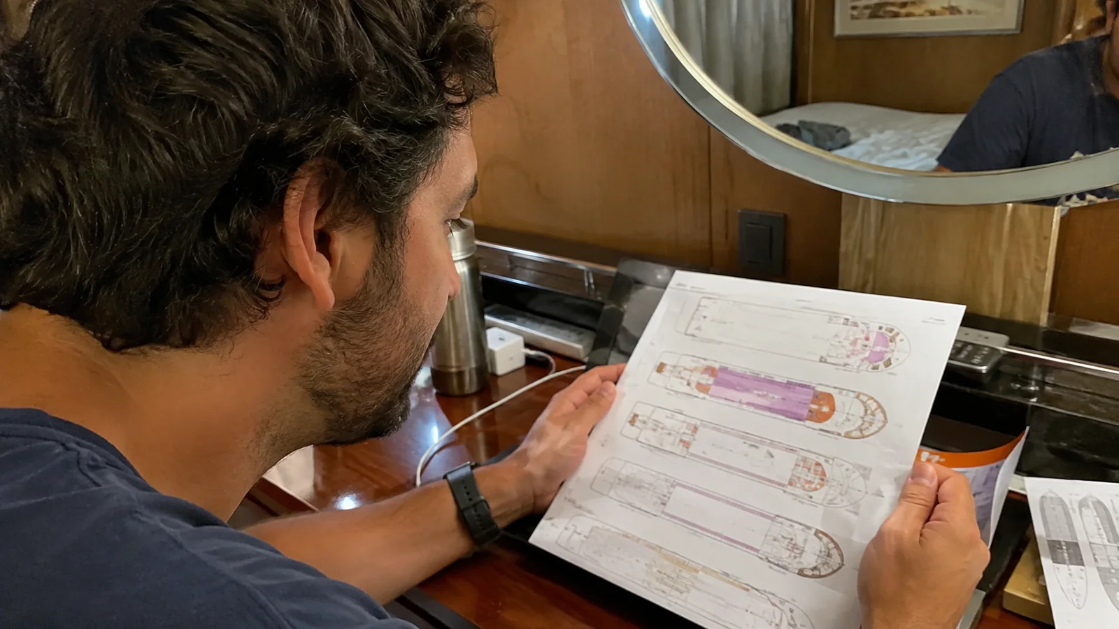 Passenger studying a printed ship deck plan at a cabin desk.