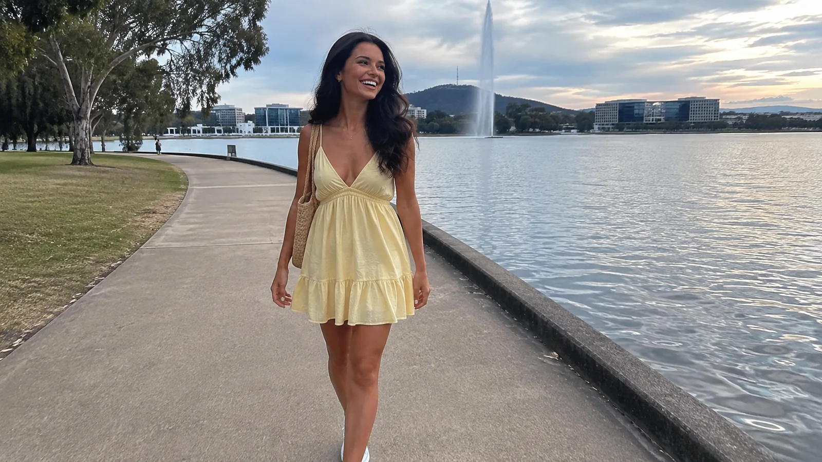 Woman walking a lakeside promenade near a tall fountain.