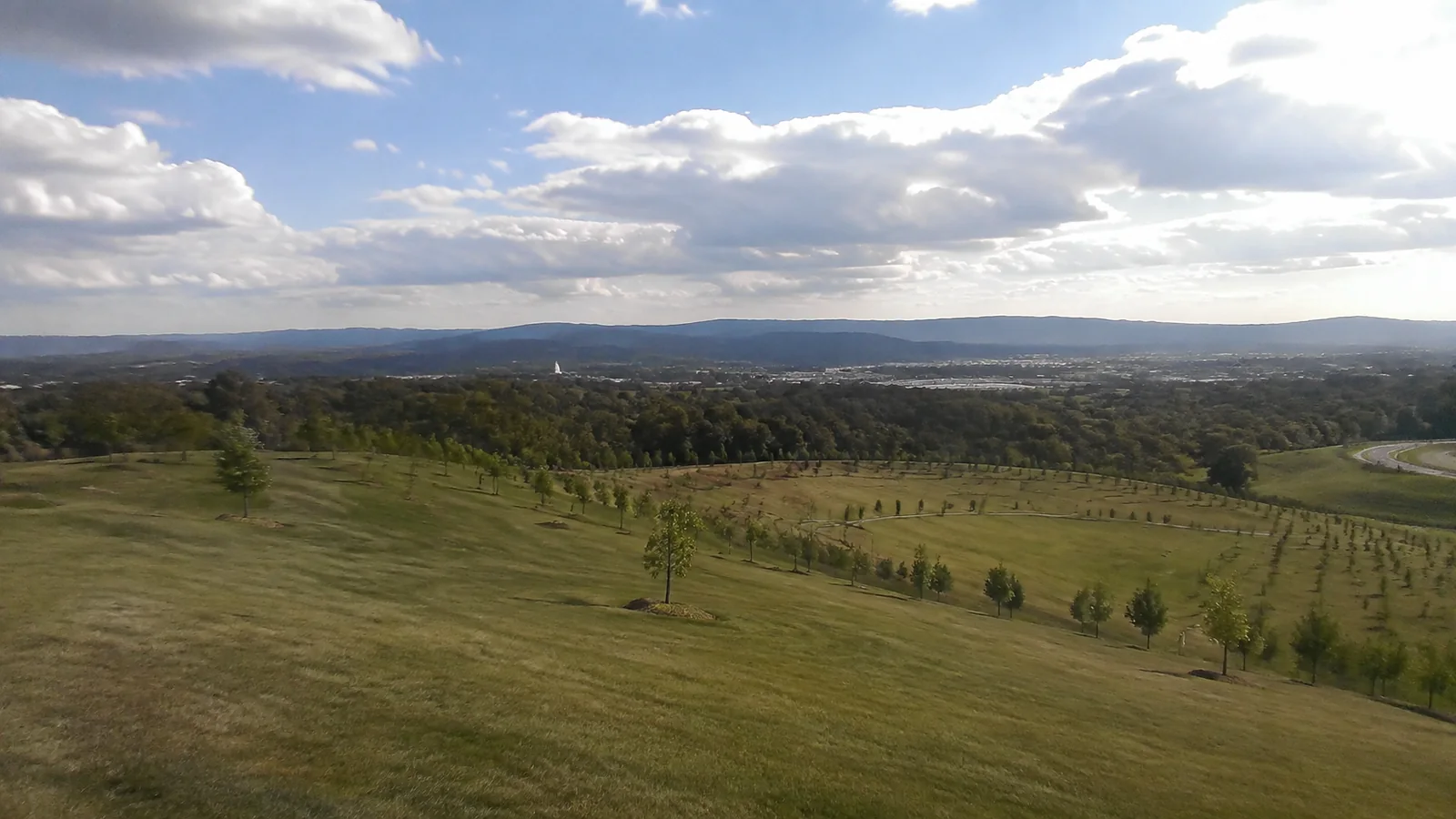 Green rolling parkland and scattered trees overlooking a distant city.