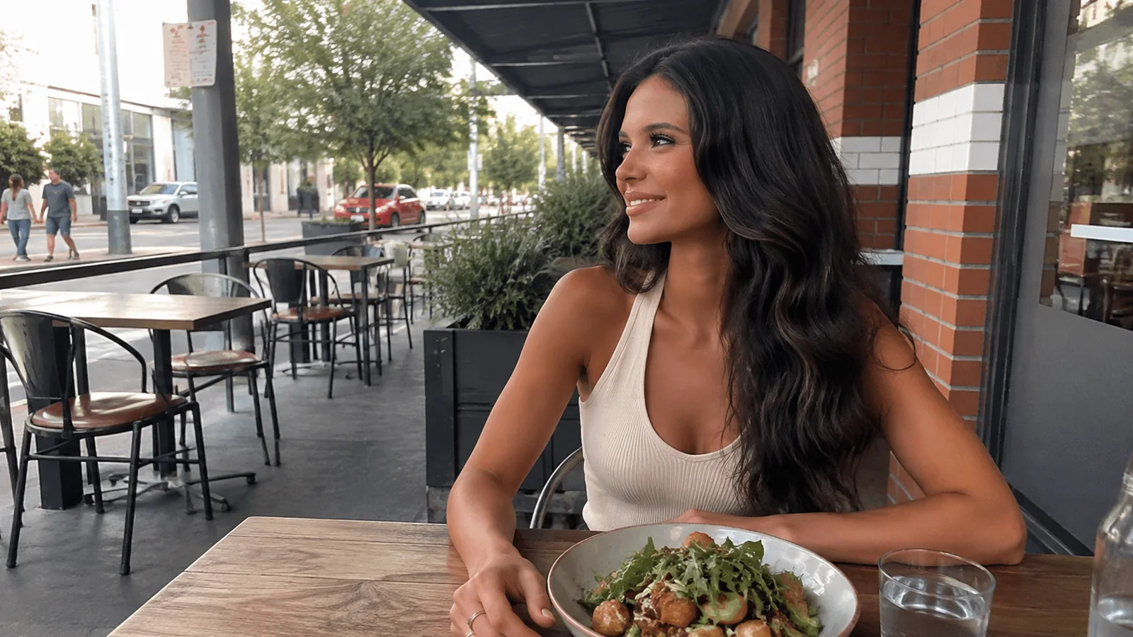 Woman eating at an outdoor cafe beside a brick building.