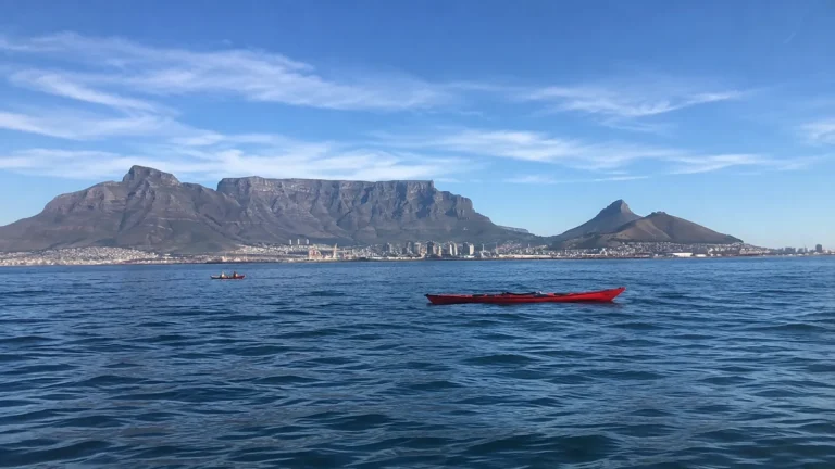 Red kayak on blue water below a broad flat-topped mountain.