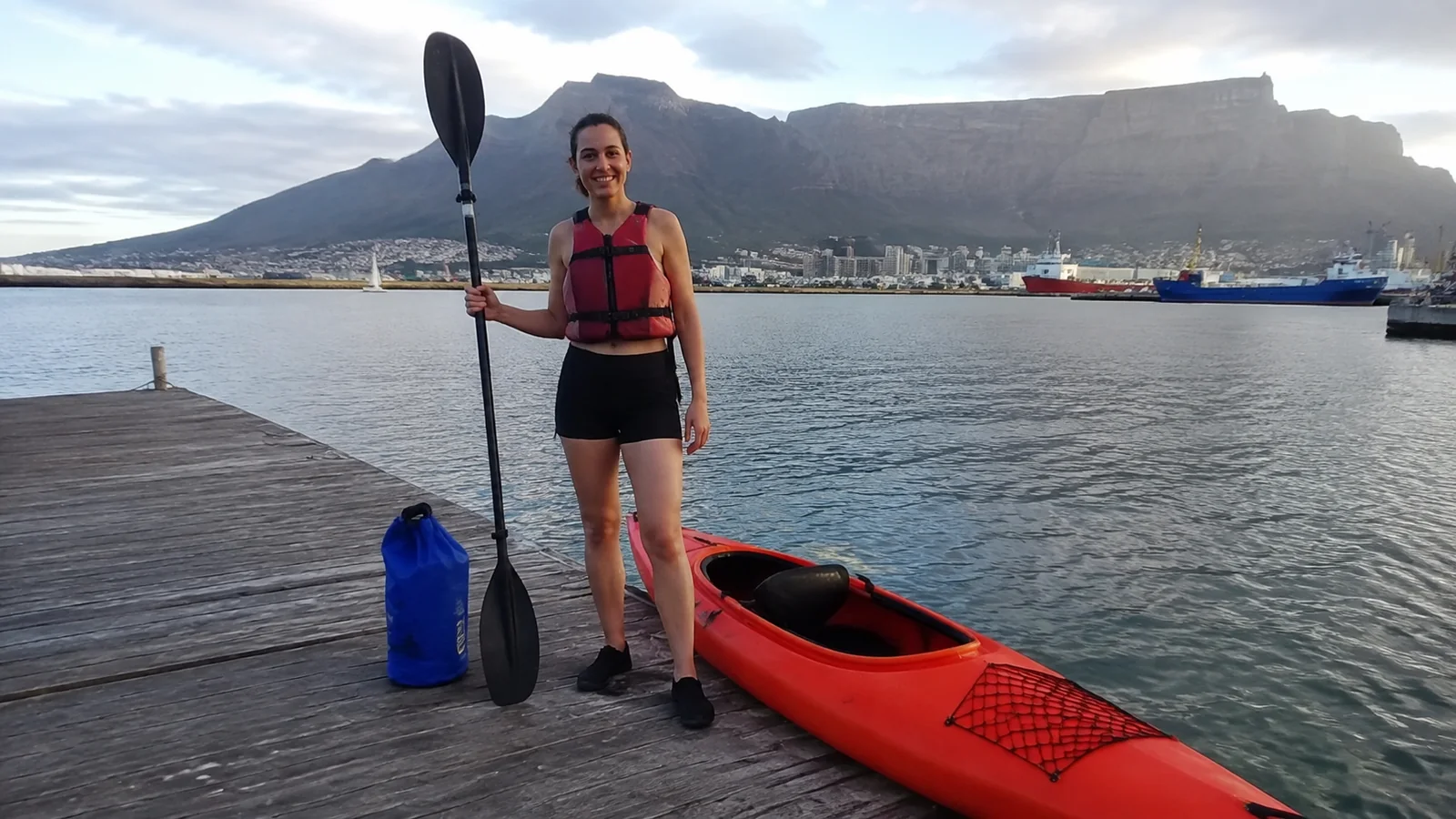 Woman holding a paddle beside a red kayak on a dock.