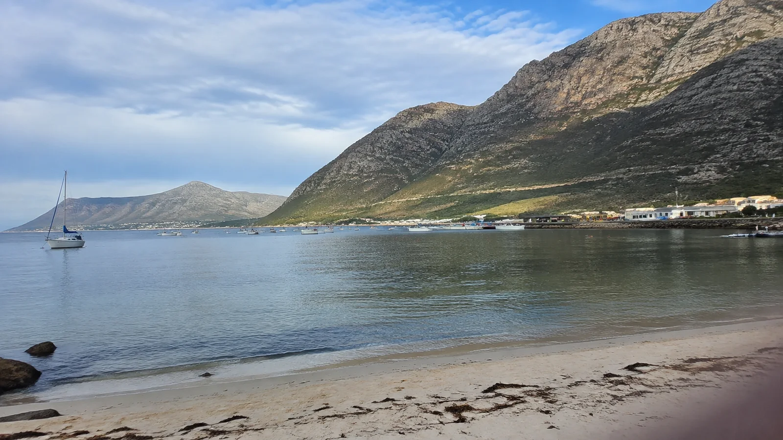 Sheltered coastal bay beneath steep rocky mountains with scattered waterfront buildings.