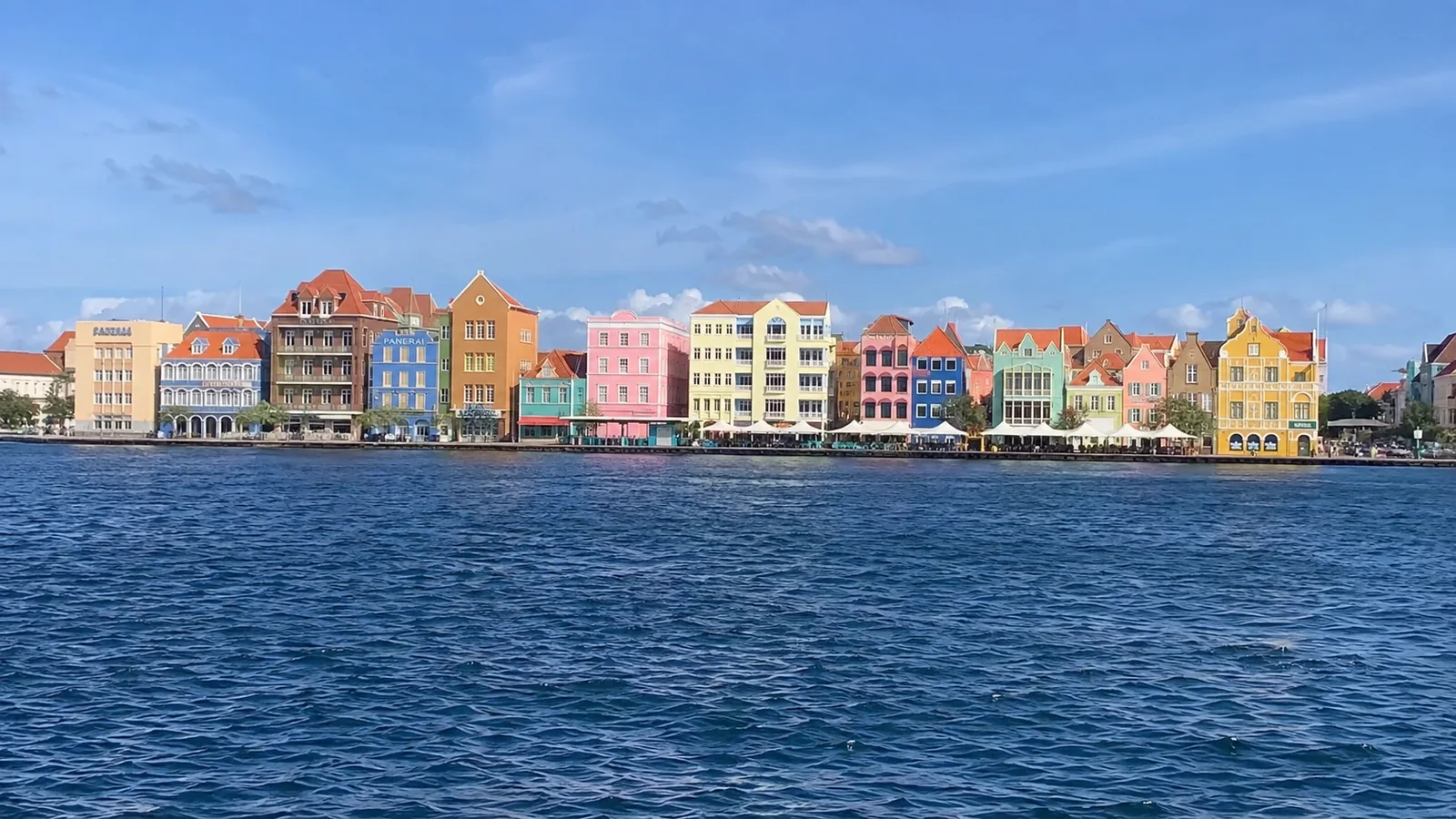 Row of colorful gabled waterfront buildings across deep blue water.