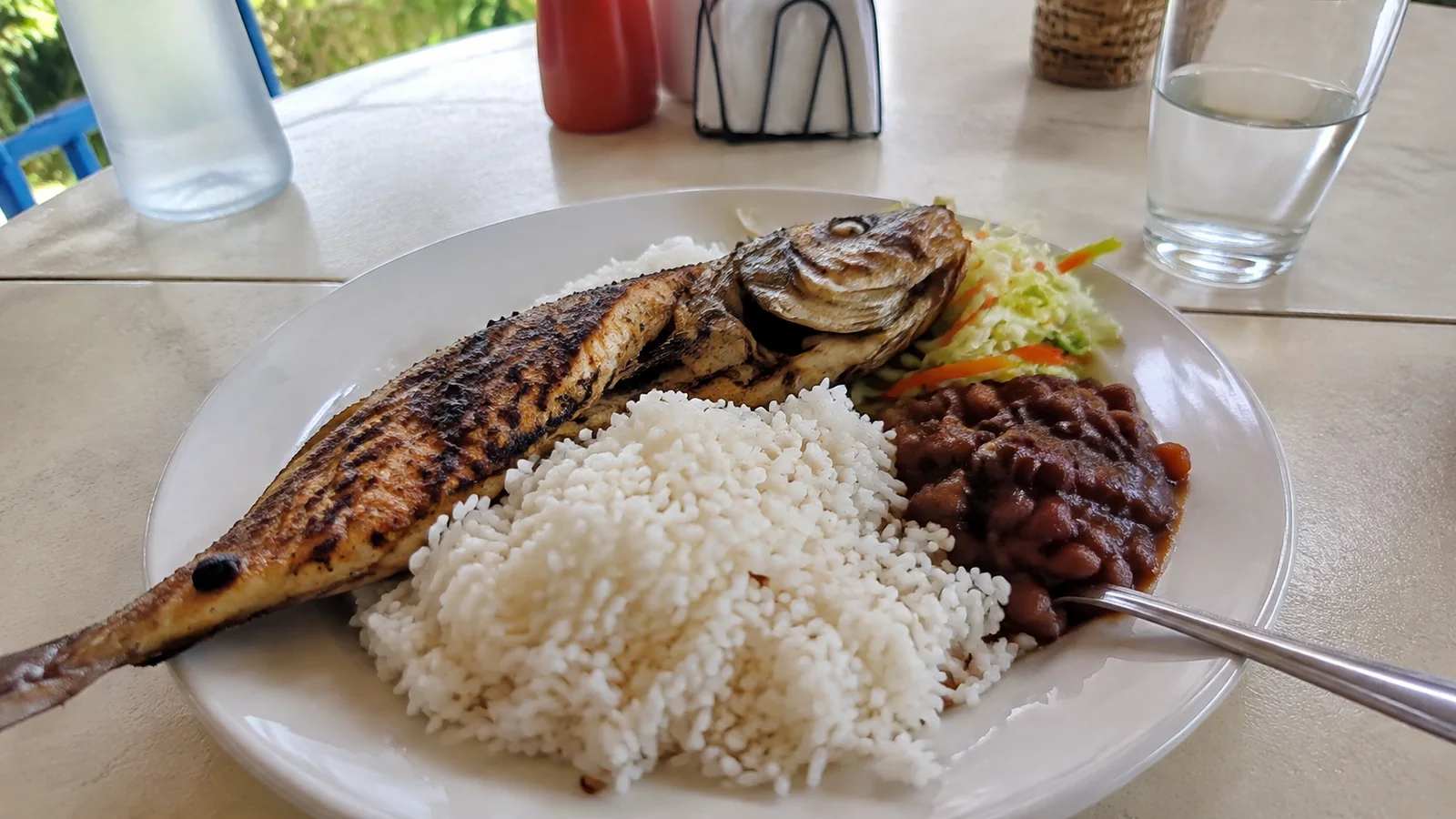 Whole grilled fish served with rice, beans, and salad.