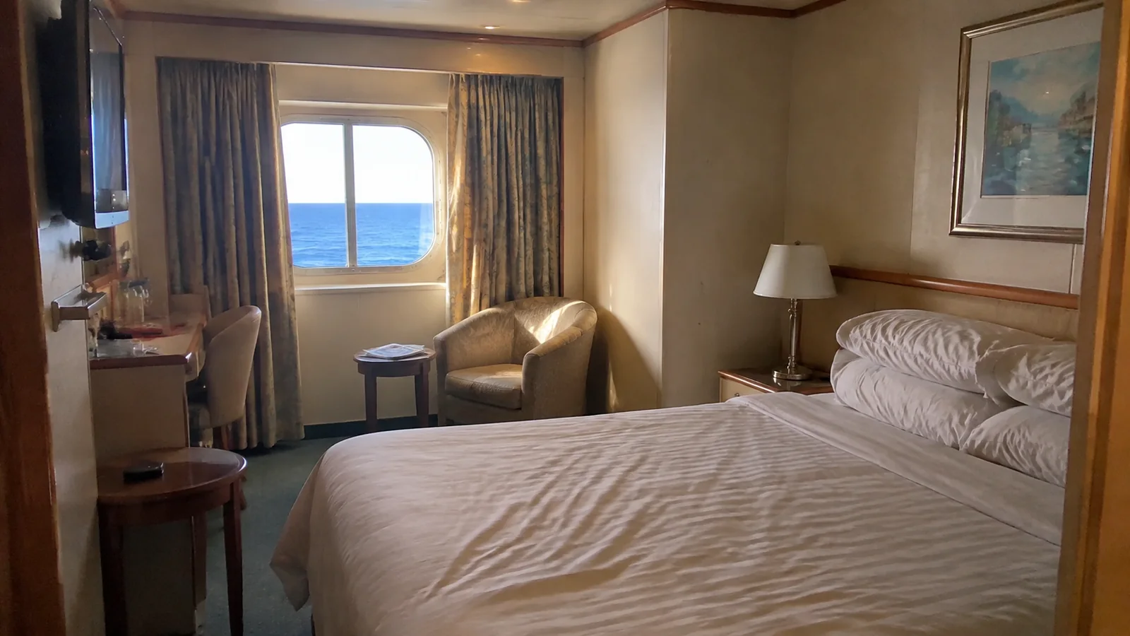 Double bed and armchair sit beside a small ocean window.