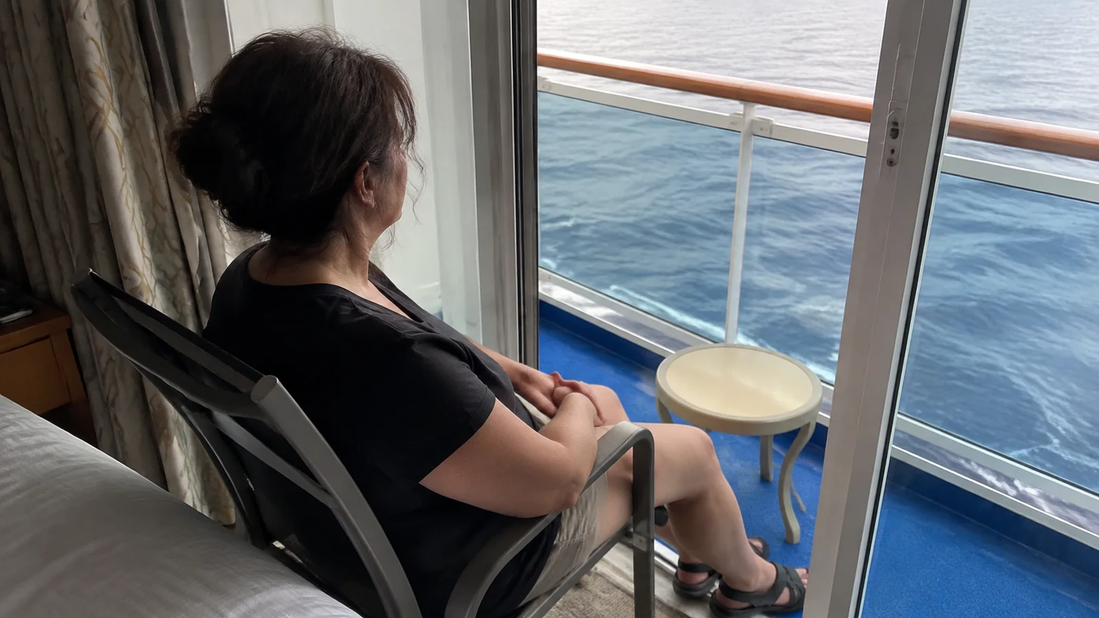Woman sits near an open balcony doorway overlooking the water.