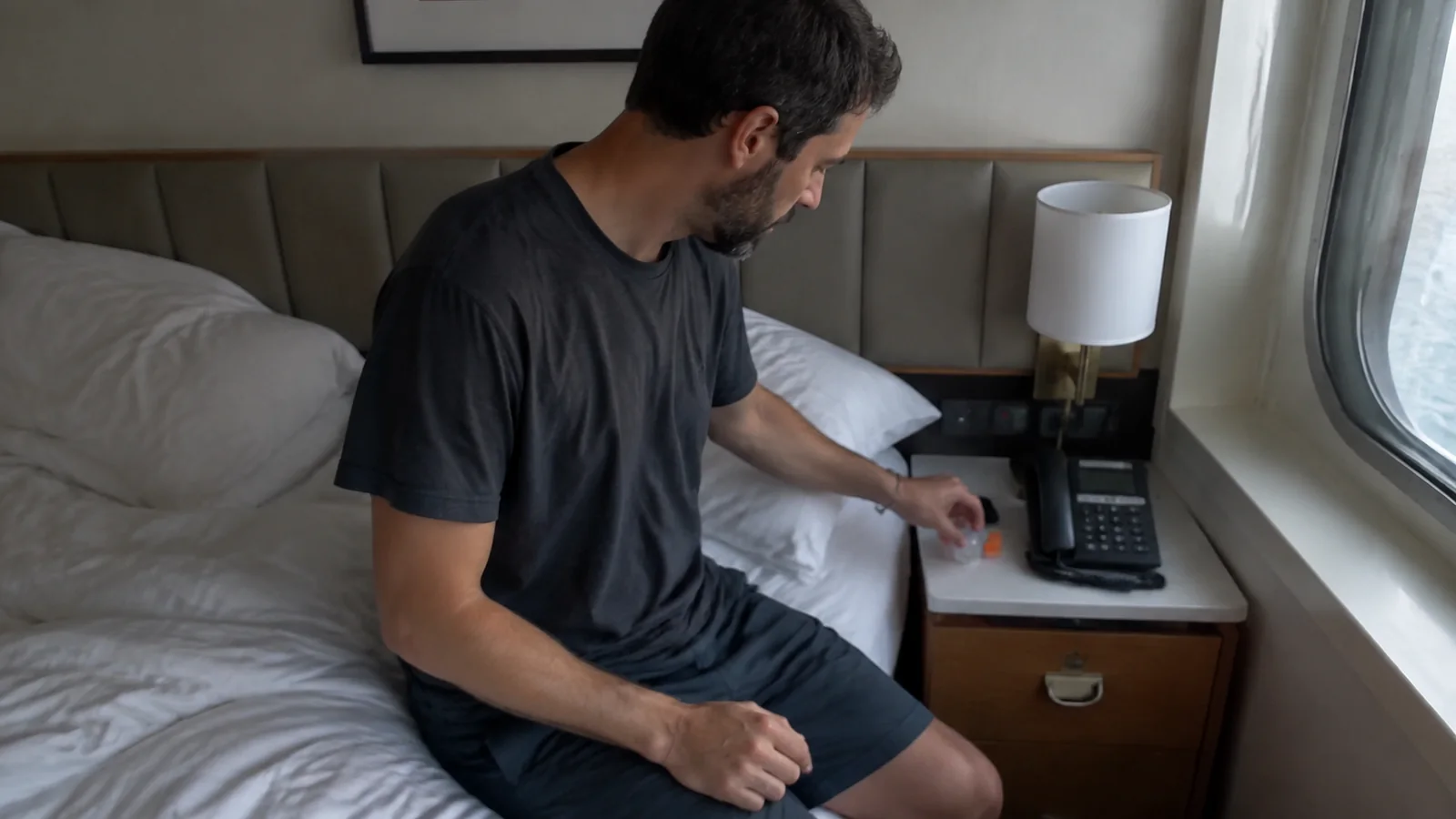 Man reaches toward a small item beside a cabin telephone.
