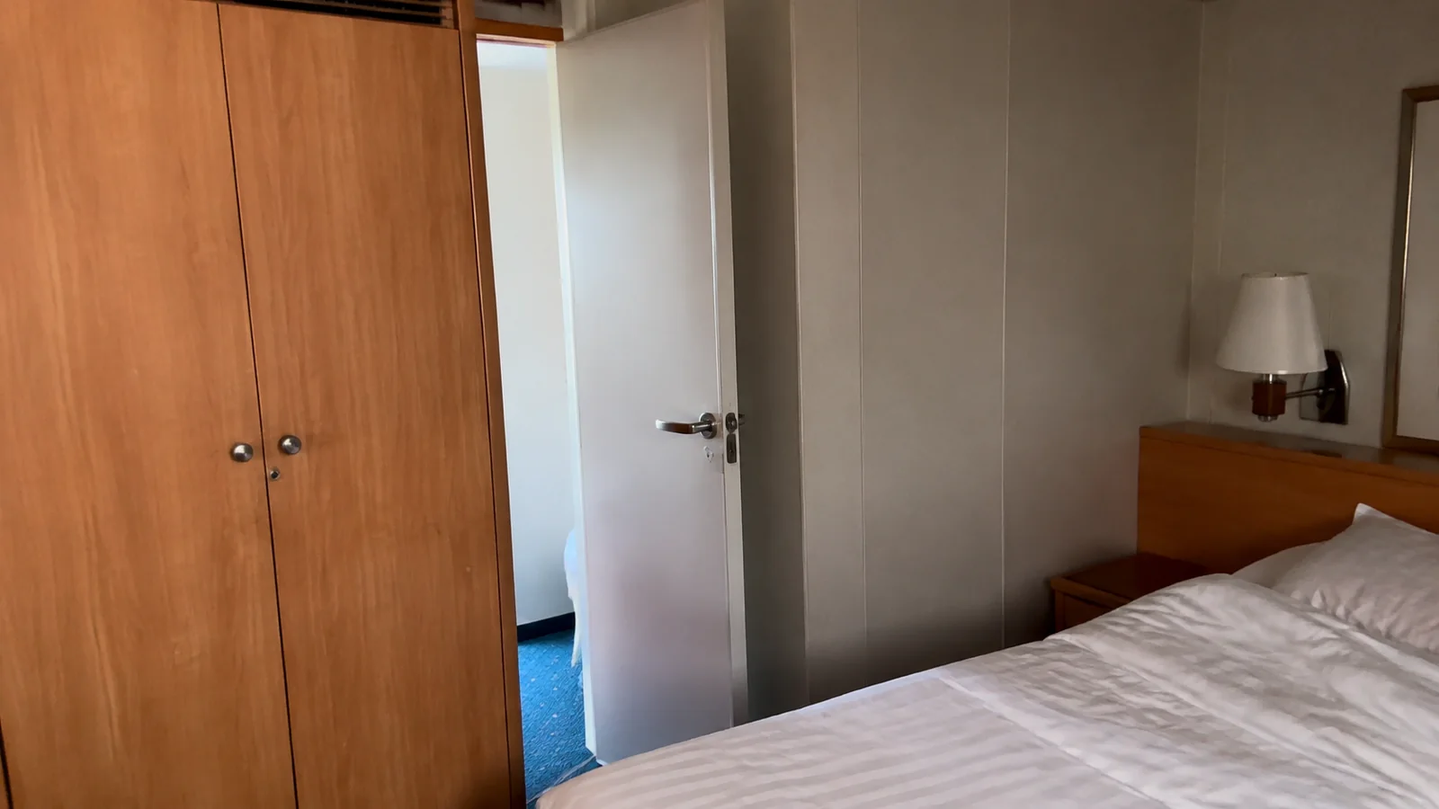 Partly open interior door stands beside a bed and wardrobe.