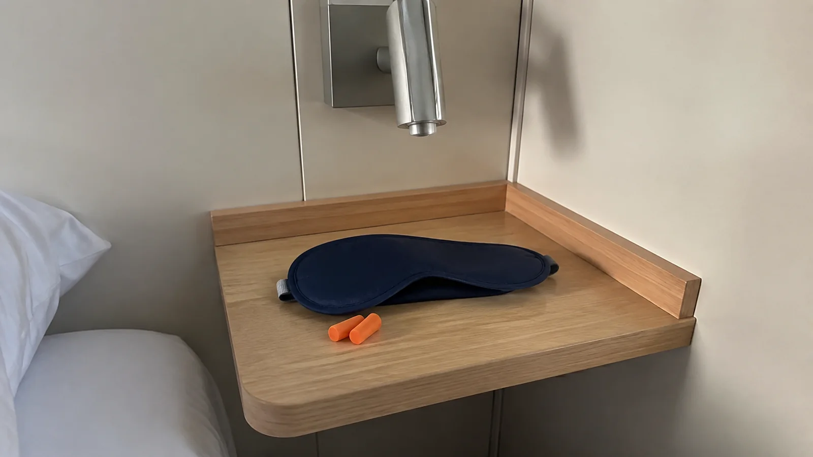 Blue sleep mask and orange earplugs on a wooden bedside shelf.