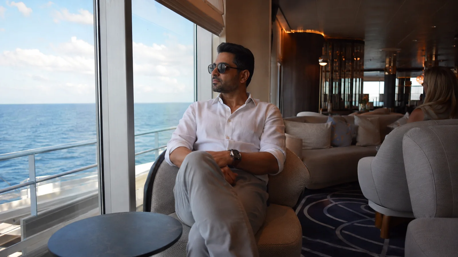 Passenger in a white shirt and trousers relaxing in an ocean-view ship lounge.