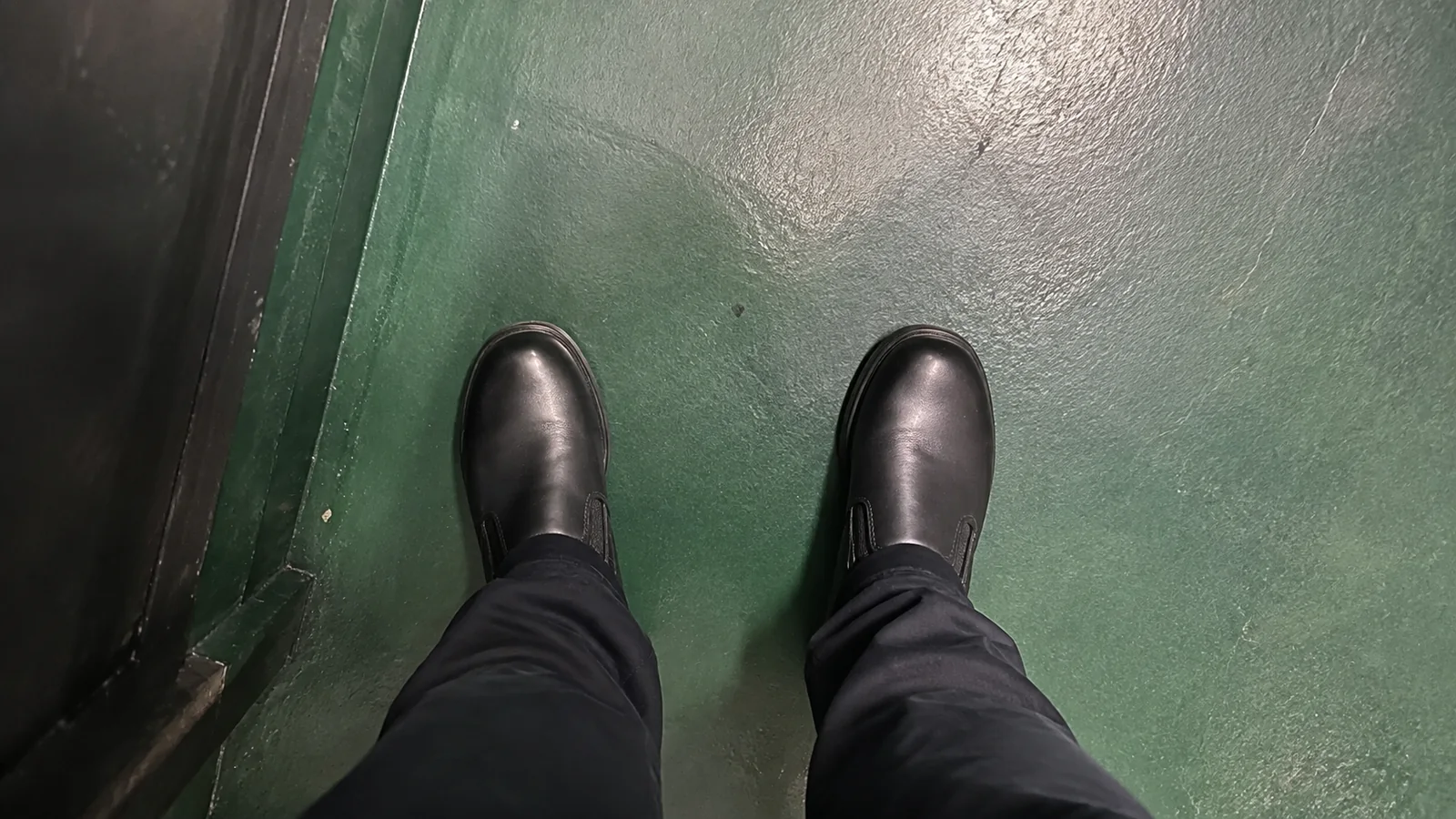 Black leather shoes and dark trousers viewed from above.