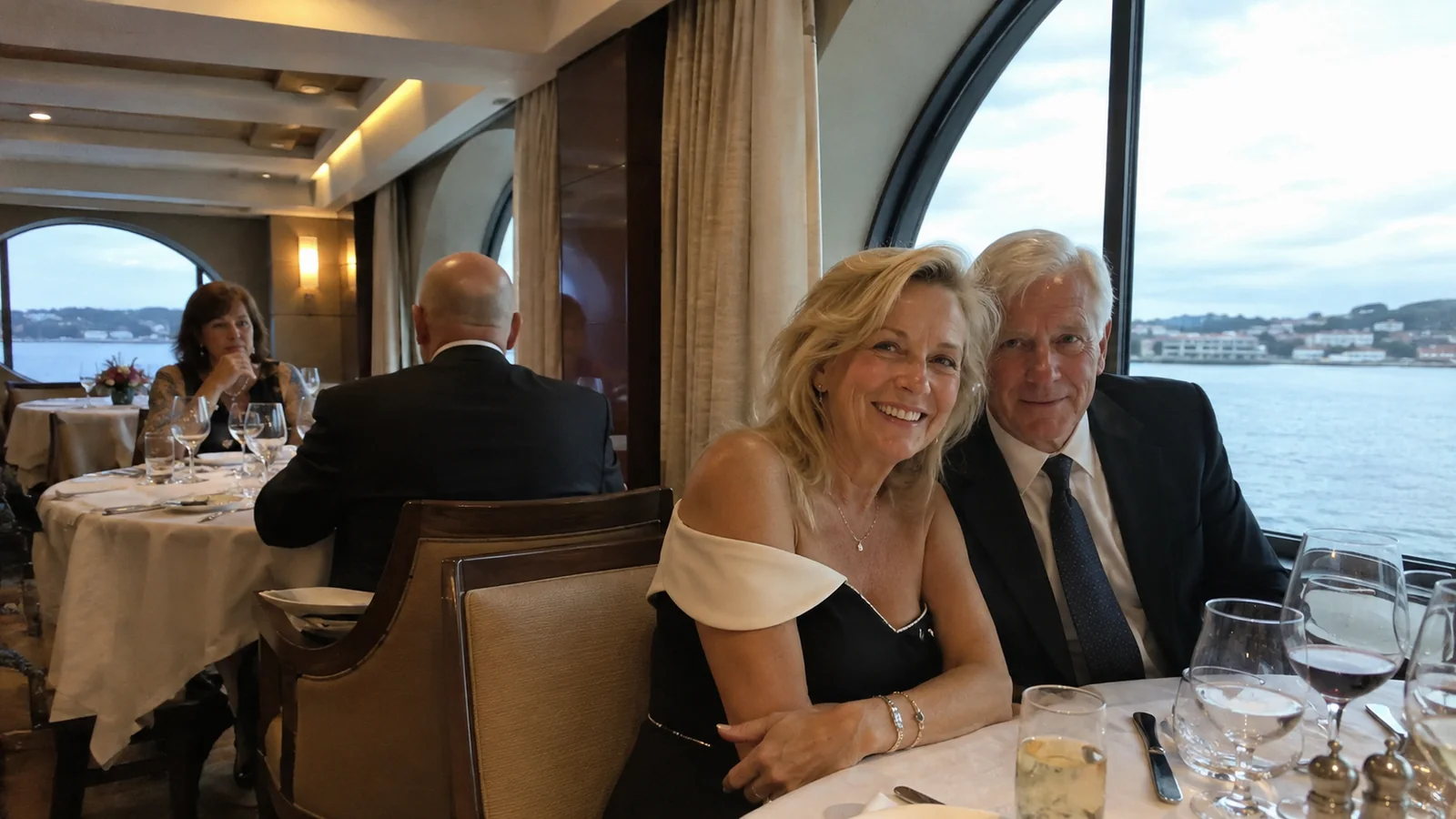 Couple dressed for dinner seated at a table beside a ship window.