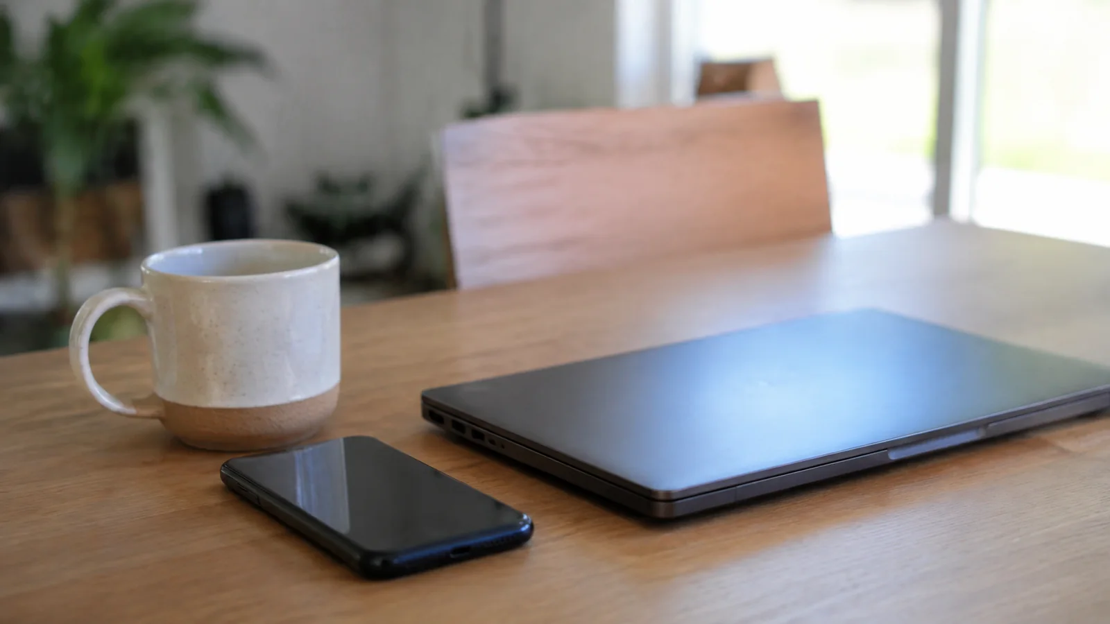 Closed laptop, smartphone and mug arranged on a wooden table.