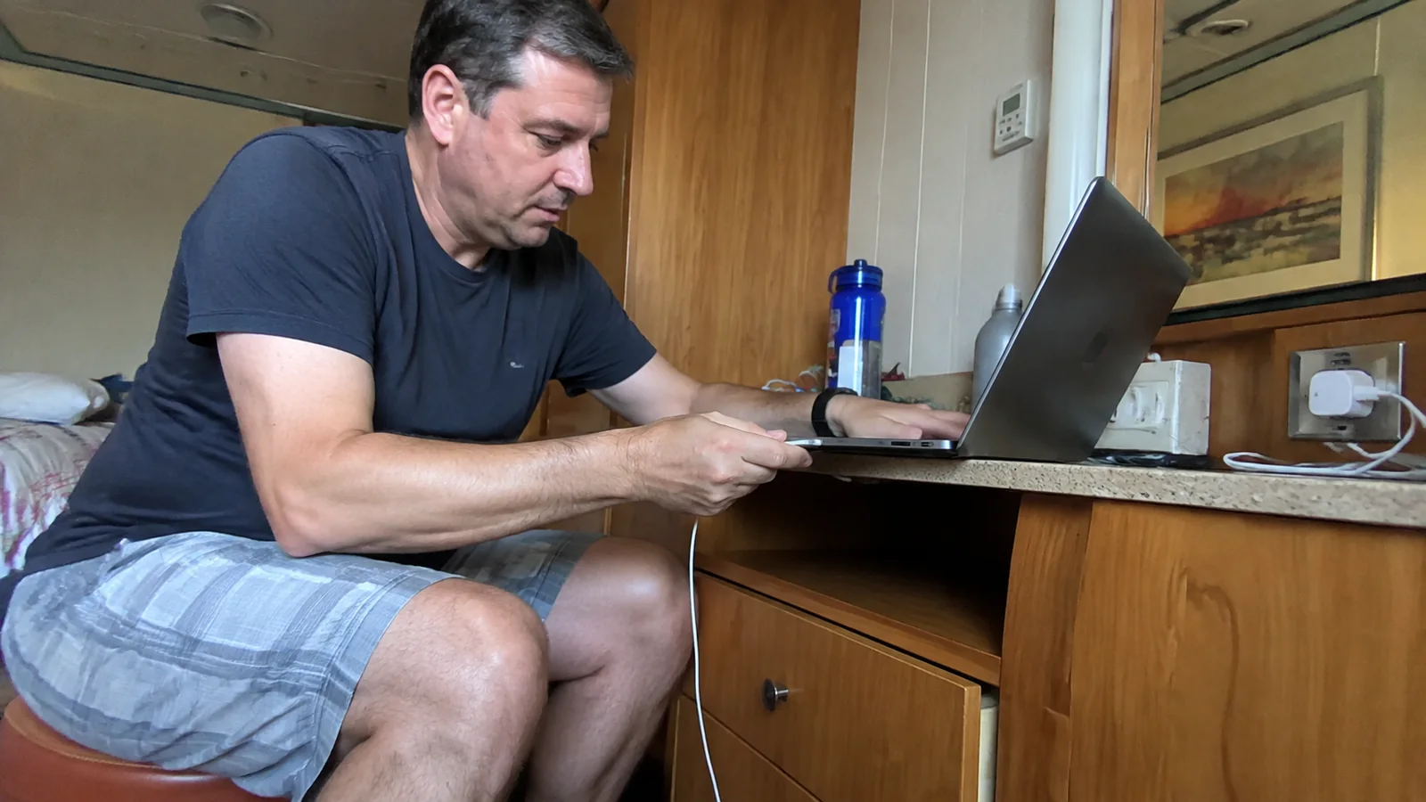 Passenger working on a laptop at a cruise cabin desk.