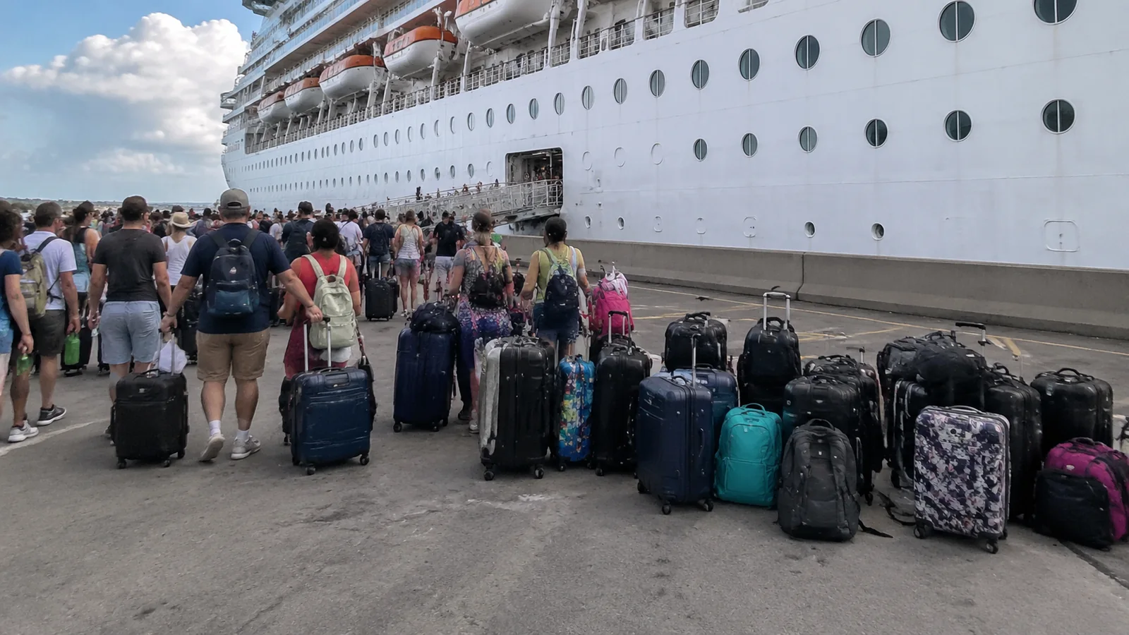 Passengers and rows of luggage beside a cruise ship