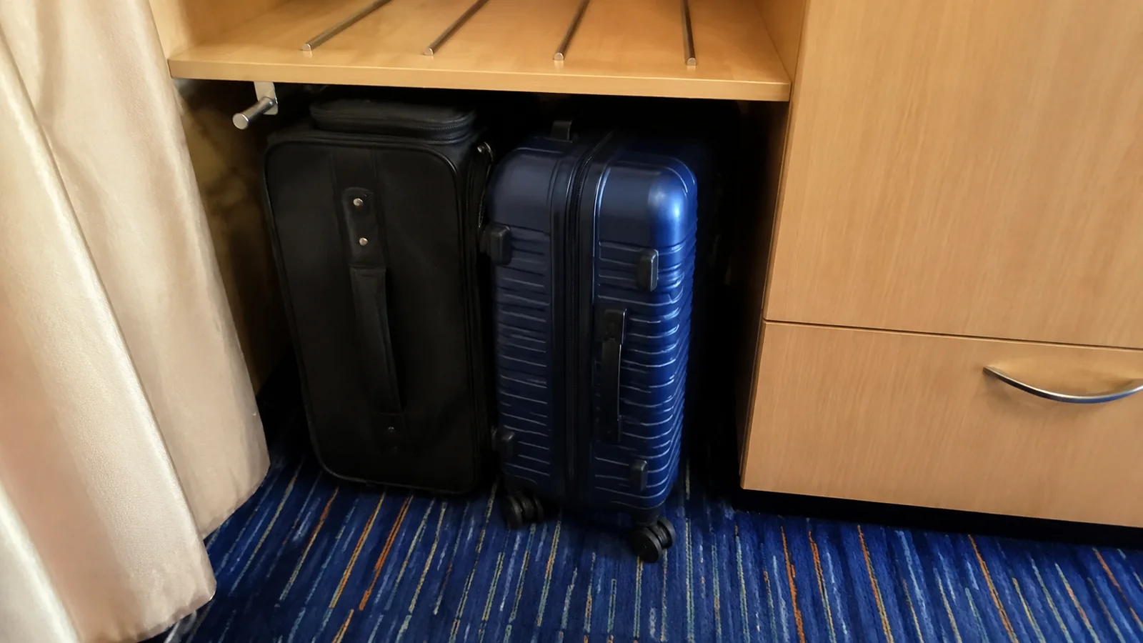 Two suitcases stored beneath a cruise cabin desk