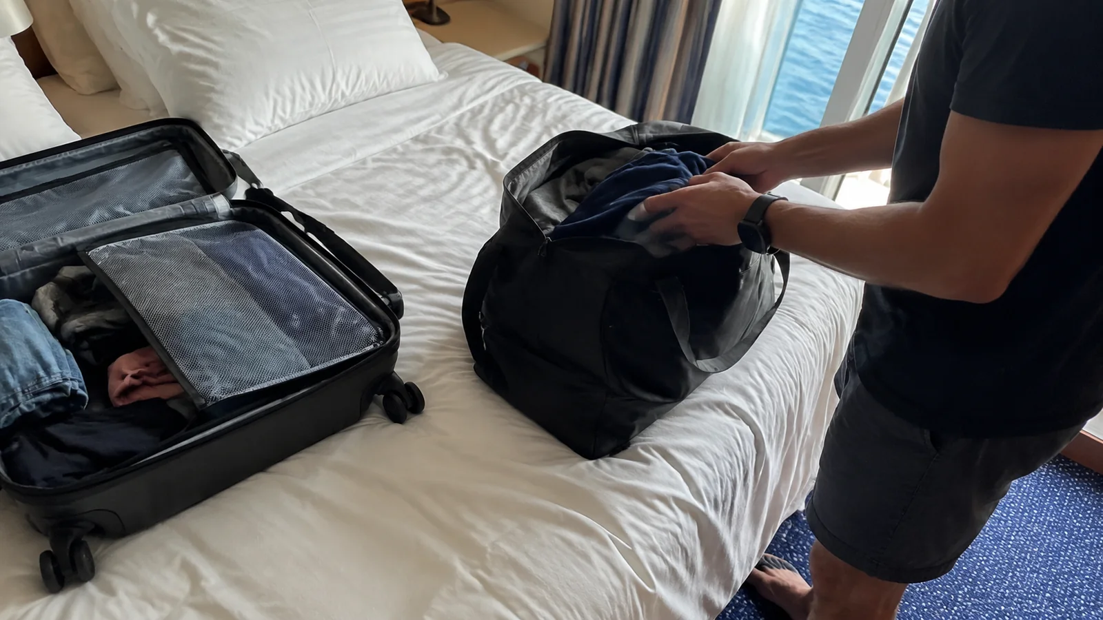 Person packing an open suitcase on a cruise cabin bed
