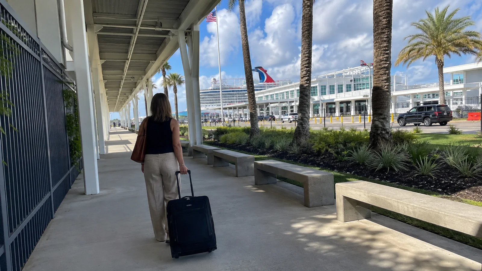 Woman pulling a suitcase along a covered cruise terminal walkway