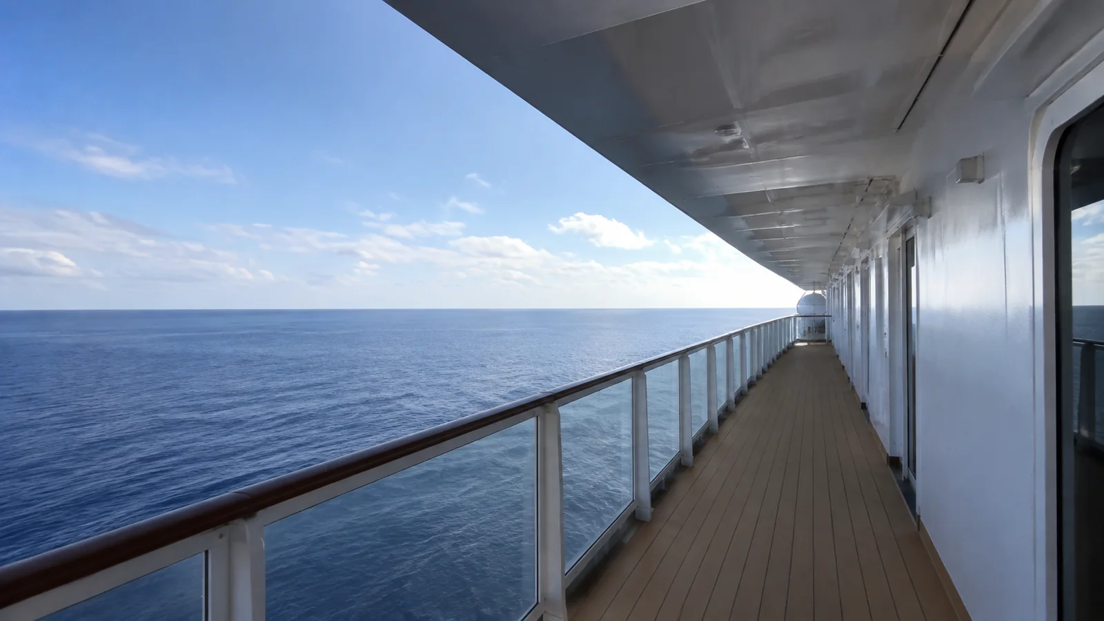 Long empty ship promenade runs beside calm blue water.