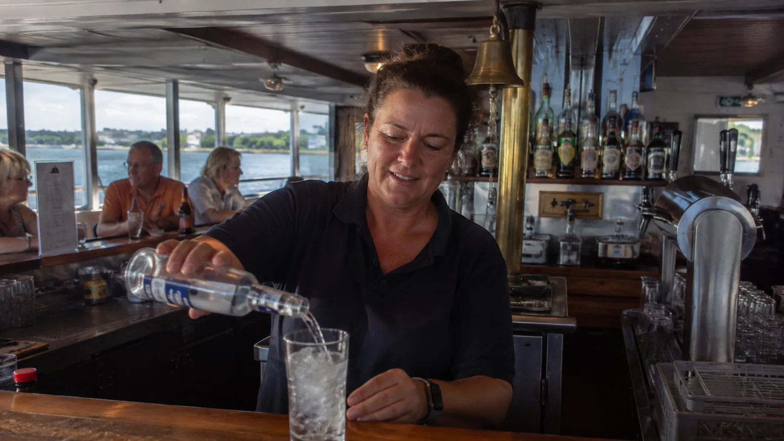 Bartender pouring bottled water into a glass at a ship bar.