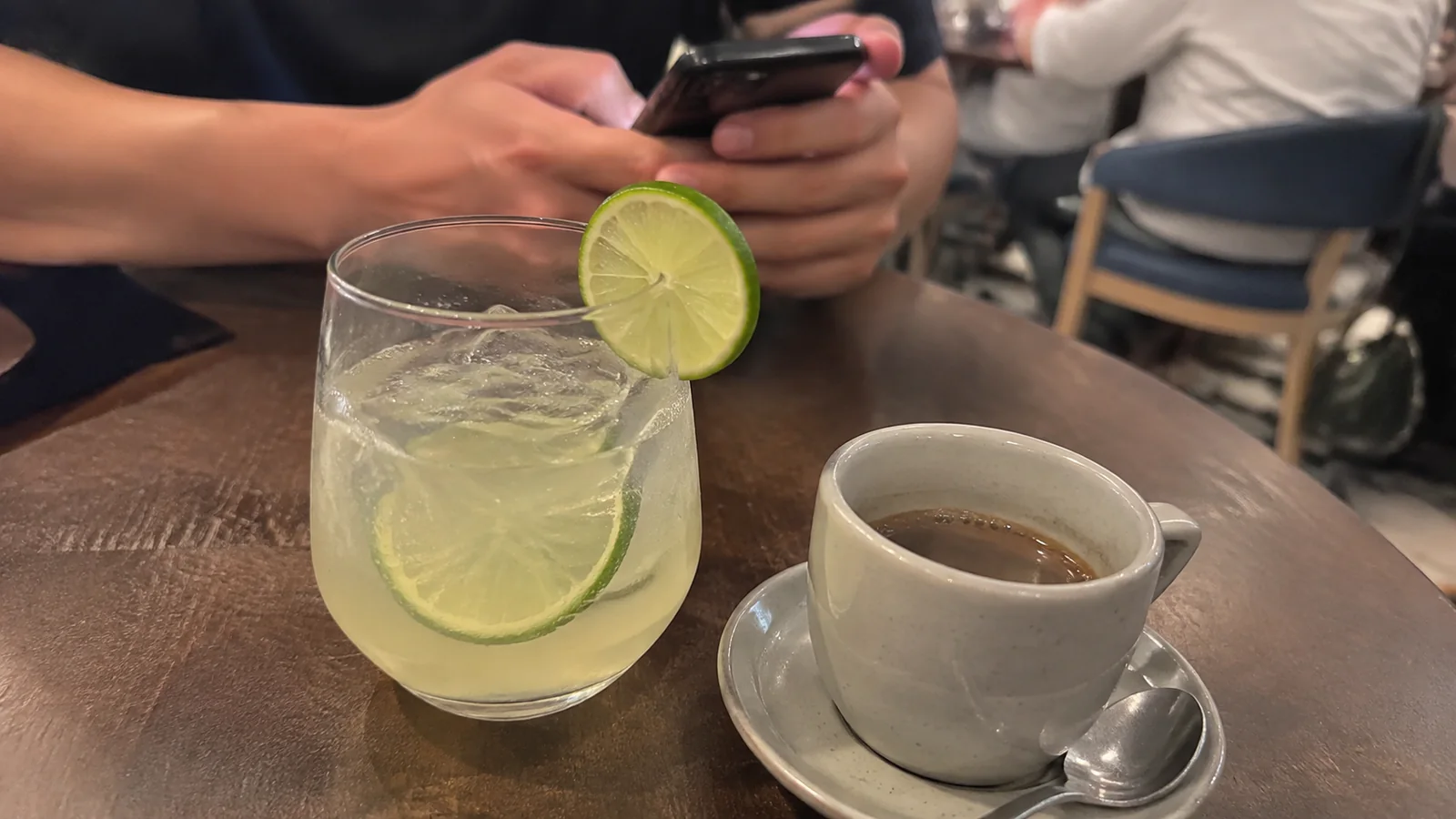 Lime drink and espresso beside a passenger using a phone.