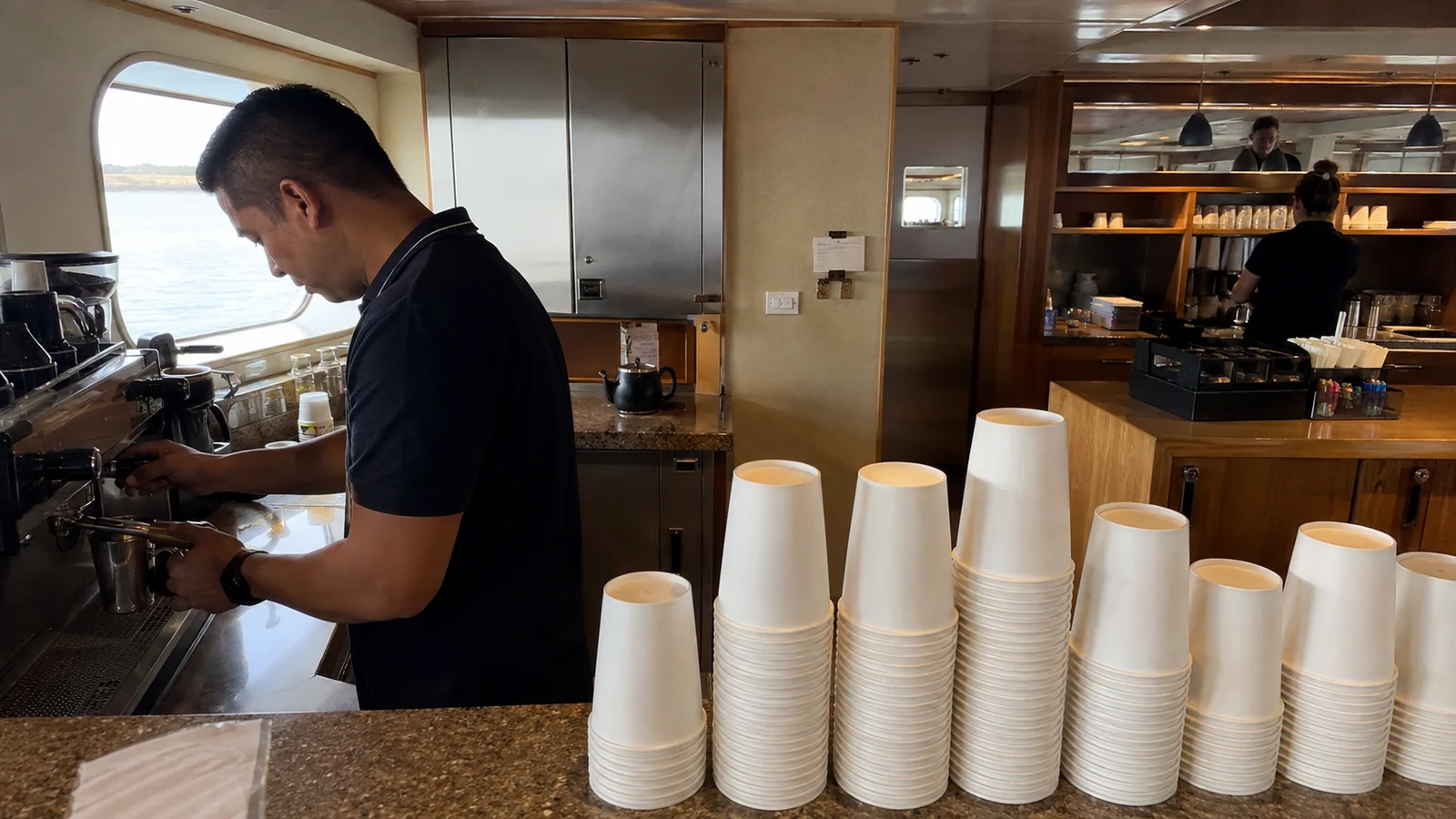 Crew member preparing coffee behind a counter with stacked paper cups.