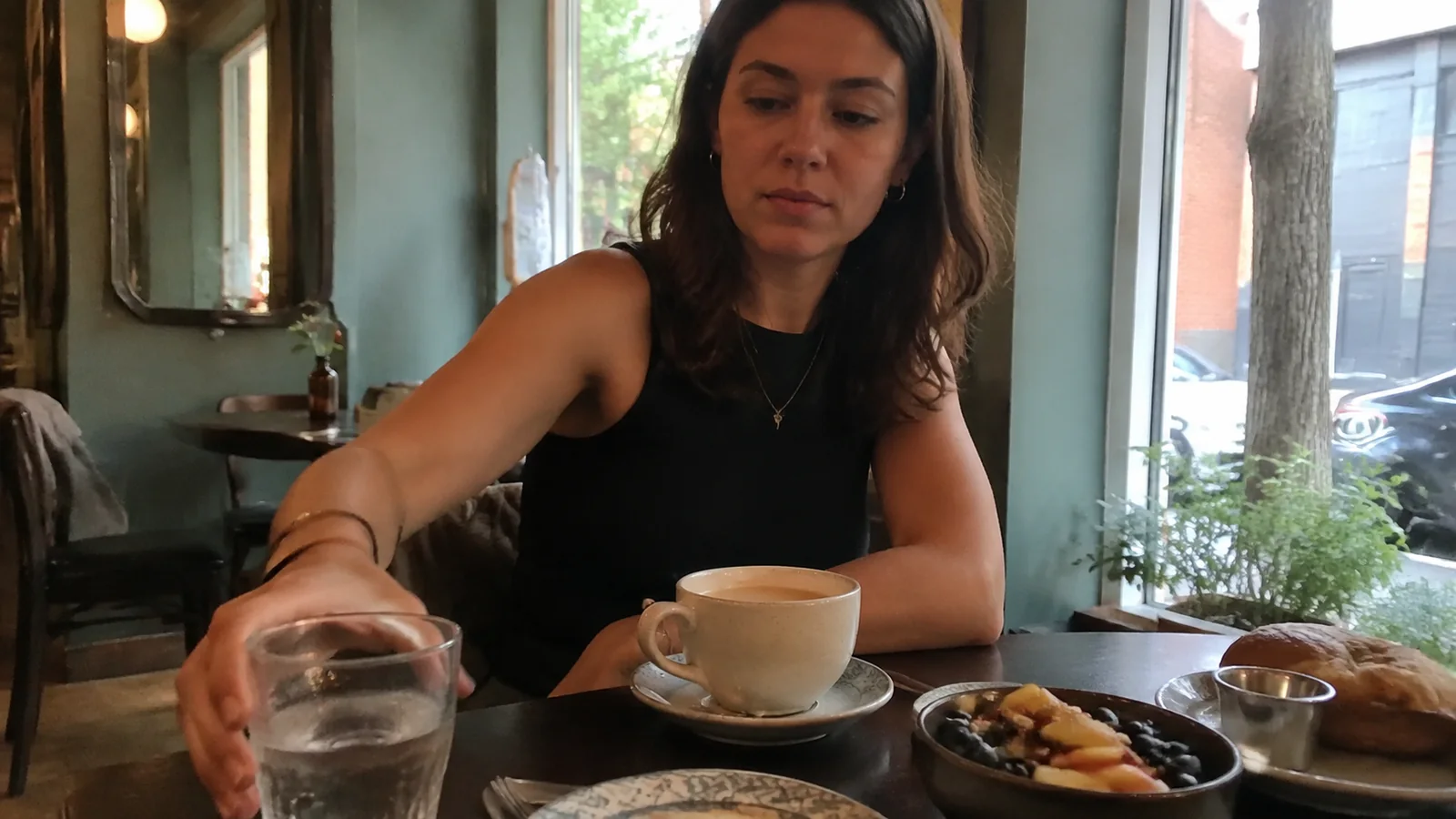 Woman reaching for a glass of water at a breakfast table.